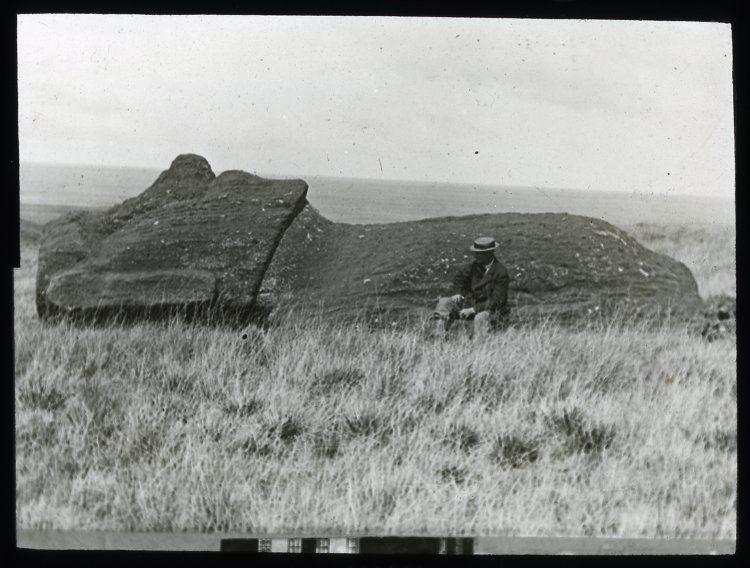 A moai lying on the ground, face upwards; on the moai statue road(?), with a White man wearing a hat and a moustache, sitting in front of it, for scale; Oc,G.T.1762, Mana Expedition to Easter Island, British Museum.jpg