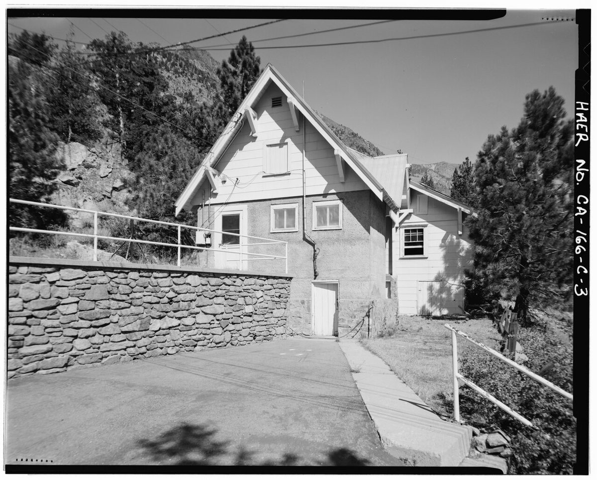 EXTERIOR OF SOUTH END OF BUILDING 104 SHOWING PAVED VEHICLE ACCESS AND ROCK RETAINING WALL CAPPED BY METAL HANDRAIL. BOTH BASEMENT DOORS (BELOW KITCHEN WINDOWS AT PHOTO CENTER HAER CAL,26-JULA.V,1C-3.tif